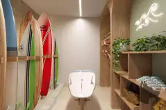 Sala de guarda-prancha com pranchas coloridas apoiadas em rack de madeira e luminária neon de onda — Upside Beach em Ponta das Canas, Florianópolis