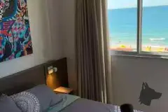 Quarto de casal com cama, cabeceira de madeira, quadro colorido e janela com vista para o mar — Upside Beach em Ponta das Canas, Florianópolis