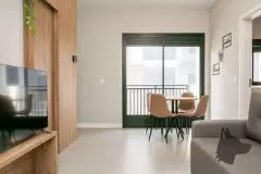 Sala integrada com TV, painel de madeira, mesa de jantar redonda e porta de correr verde para varanda — Upside Beach em Ponta das Canas, Florianópolis