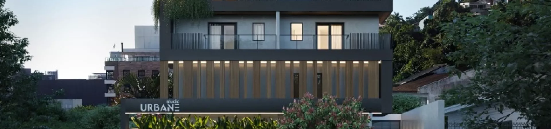 Fachada frontal do edifício ao entardecer, 3 andares com revestimento cinza e ripado de madeira, letreiro Studio Urbane iluminado e vegetação na entrada — Studio Urbane em Centro, Florianópolis