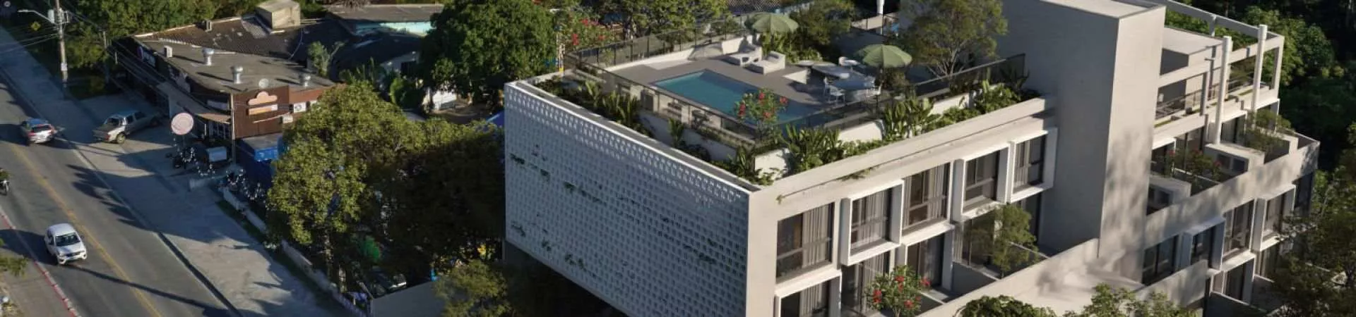 Vista aérea oblíqua do edifício Verset com fachada de treliça branca vazada, rooftop com piscina e área de lazer na esquina com a Avenida Campeche — Verset em Campeche, Florianópolis