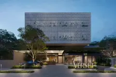 Fachada frontal do edifício Verset à noite, bloco superior de treliça branca sobressalente, lojas no térreo iluminadas e letreiro Verset — Verset em Campeche, Florianópolis