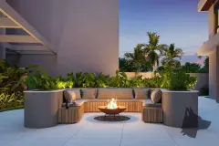 Espaço fire pit externo ao entardecer com sofá semicircular de pedra, tocha de fogo e palmeiras — Villa Maggiore em João Paulo, Florianópolis