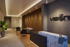 Hall de recepção com balcão de mármore, logotipo Vision na parede de concreto, sofás e planta — Vision 1617 em Saco Grande, Florianópolis