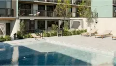 Piscina com espreguiçadeiras de madeira, cabanas com cortinas e fachada do edifício com varandas e jardins — Viva Balneário Estreito em Balneário, Florianópolis