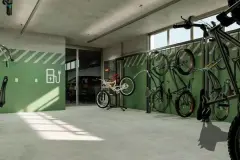 Bicicletário com bikes penduradas em parede verde, suportes verticais e sinalização de carregamento elétrico — Viva Balneário Estreito em Balneário, Florianópolis