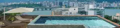 Piscina infinita no rooftop com espreguiçadeiras, guarda-sol e vista panorâmica para o skyline de Florianópolis e a Ponte Hercílio Luz — VYU One em Coqueiros, Florianópolis