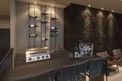 Bar com adega de vinhos em trilhos suspensos, balcão escuro arredondado e balde de gelo com garrafas — VYU One em Coqueiros, Florianópolis