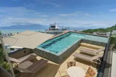 Piscina no rooftop com deck de madeira, espreguiçadeiras, mesa redonda e vista para as montanhas e o mar — VYU One em Coqueiros, Florianópolis