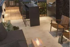 Lounge gourmet ao ar livre com lareira de etanol, mesa alta com bancos e churrasqueira à noite — VYU One em Coqueiros, Florianópolis